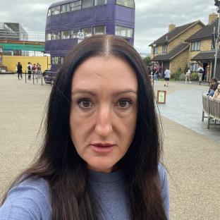 Woman with long dark hair in front of a purple bus.
