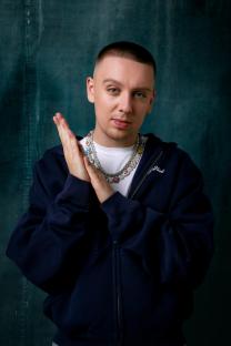 Portrait of Aitch wearing a navy zip-up hoodie and multiple necklaces.