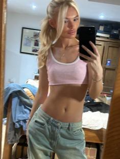 Selfie of a young woman in a pink crop top and light blue jeans.